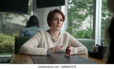 Young Woman In Conversation With Friend At Coffee Shop. Red Hair Girl Talking Sharing Information Sitting At Restaurant