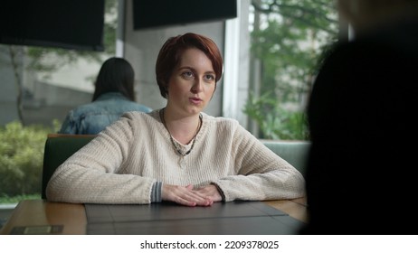 Young Woman In Conversation With Friend At Coffee Shop. Red Hair Girl Talking Sharing Information Sitting At Restaurant