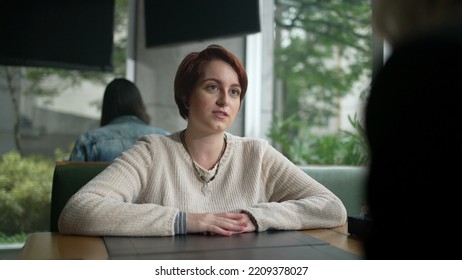 Young Woman In Conversation With Friend At Coffee Shop. Red Hair Girl Talking Sharing Information Sitting At Restaurant