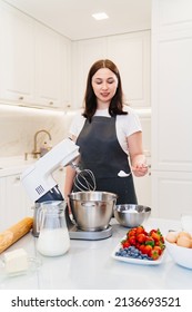 A Young Woman Cook Adds A Spoonful Of Flour To Prepare Dough In A Mixer Bowl. Cooking Courses. Bread And Dessert Recipes. Family Business. Online Lessons For Cooks.