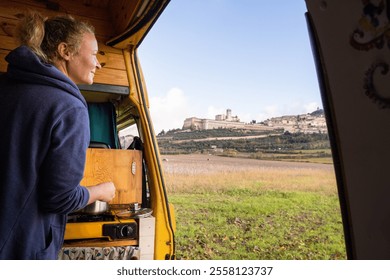 Young woman cooking breakfast in vintage camper van near Assisi hilltop town in Umbria, Italy - Powered by Shutterstock