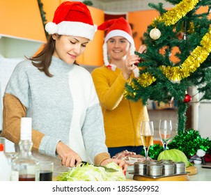 Young Woman In Cooking Christmas Dinner At Home, Sister Decorating Christmas Tree