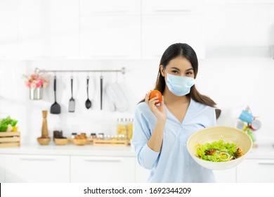 Young Woman Cooking Delicious Food In The Kitchen And Wearing Face Protection Mask To Anti Saliva, Cough. Stay At Home During The COVID-19 Self-quarantine 14 Days.