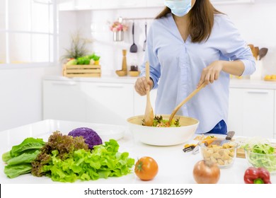 Young Woman Cooking Delicious Food In The Kitchen And Wearing Face Protection Mask To Anti Saliva, Cough. Stay At Home During The COVID-19 Self-quarantine 14 Days.