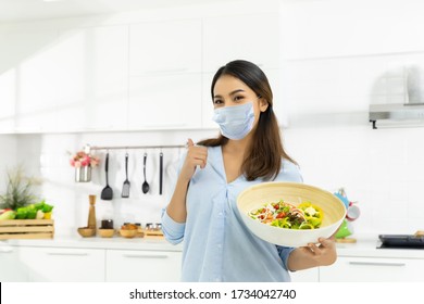 Young Woman Cooking Delicious Food In The Kitchen And Wearing Face Protection Mask To Anti Saliva, Cough. Stay At Home During The COVID-19 Self-quarantine 14 Days.