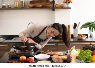Young woman cooking a hamburger in kitchen with a smile and delicious