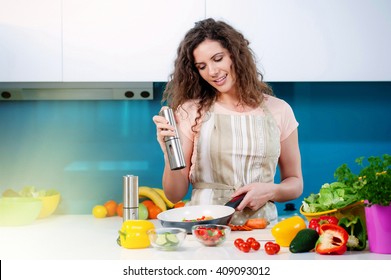 Young Woman Cooking Healthy Food, Pouring Salt In A Pan With Vegetables In It.