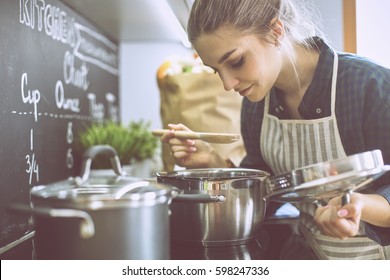 Young woman cooking in her kitchen standing near stove - Shutterstock ID 598247336