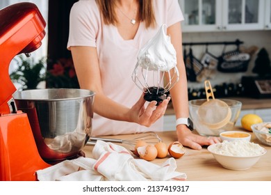 Young woman cooking meringue in the kitchen of her home. Process of cooking meringue. Whipped egg whites on mixer whisk on linen towel over gray texture background. Baking dessert concept. Close up