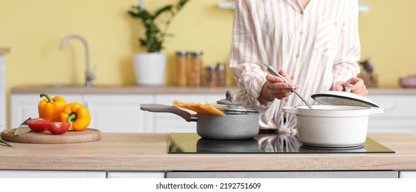 Young Woman Cooking On Modern Electric Stove In Kitchen