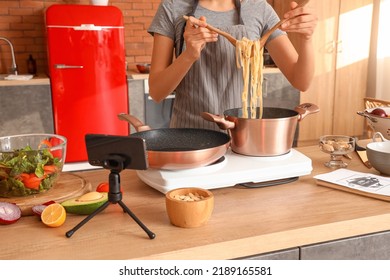 Young Woman Cooking Pasta While Watching Video Tutorial In Kitchen