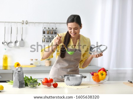 Young woman cooking tasty soup in kitchen