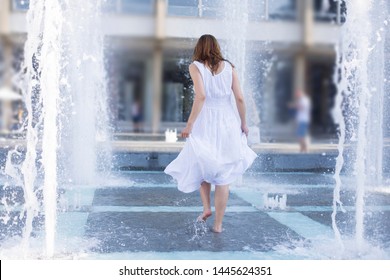 Young Woman Cooling Down In Fountain Water Spray During Summer Heat