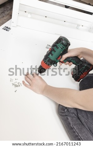 Young woman with cordless screwdriver assembling white folding table on the floor