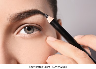 Young Woman Correcting Eyebrow Shape With Pencil, Closeup