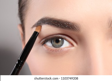 Young Woman Correcting Eyebrow Shape With Brush, Closeup