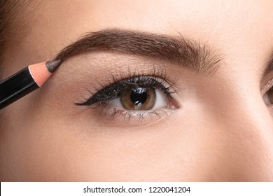 Young Woman Correcting Shape Of Eyebrow With Pencil, Closeup