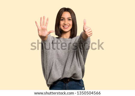 Young woman counting six with fingers on isolated yellow background