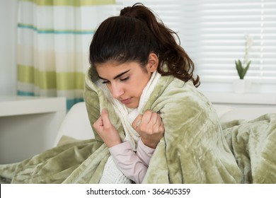 Young woman covered with blanket suffering from cold at home