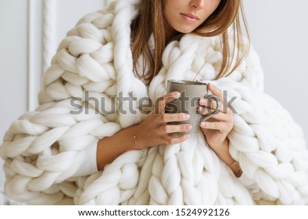 Young woman covered with chunky merino wool blanket on white background. Cozy winter style.