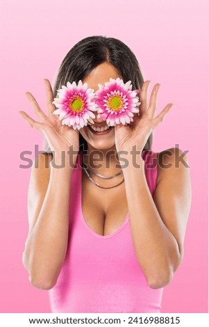 Young woman covering eyes with flowers with pink shirt on a pink background.