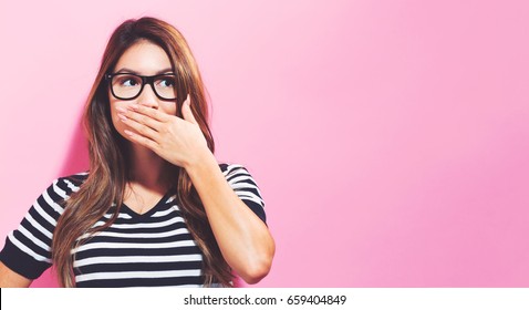 Young woman covering her mouth on a pink background