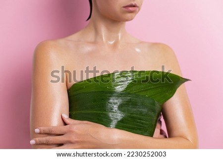 young woman covers her breasts with a green leaf of a tropical plant in summer on a pink background. ecological healthy weight loss of a person