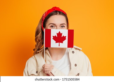 A young woman covers her face with a small flag of Canada, Canada Day celebration. Student girl holding the flag of Canada, education abroad