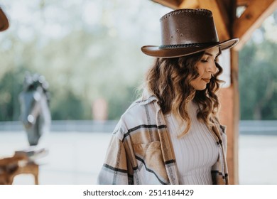 Young woman in cowboy hat and plaid shirt standing in a serene outdoor setting, exuding tranquility and rustic charm. - Powered by Shutterstock