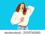 A young woman in a cozy sweater yawns while holding coffee against a vibrant blue backdrop in a playful moment