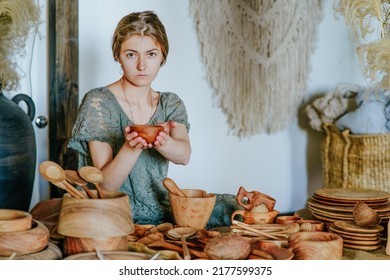 Young woman crafter holding handmade wooden cup in her workshop with eco natural tableware. Woodcraft local small business concept. Selective focus.