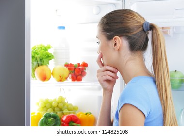 Young Woman Craving Food Choosing Near Refrigerator