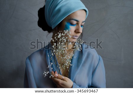 young woman with creative make up in light blue gown holding fragile white flowers