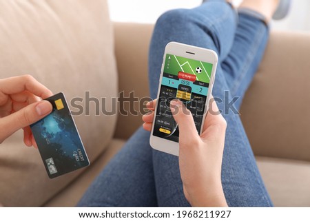 Young woman with credit card placing sports bet at home