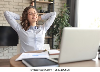 Young woman crossed hands behind head, enjoying break time at home. Peaceful carefree business woman resting at table with computer, looking aside, dreaming of future. - Shutterstock ID 1851102505