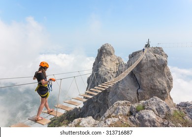 Young Woman Crossing The Chasm On The Rope Bridge