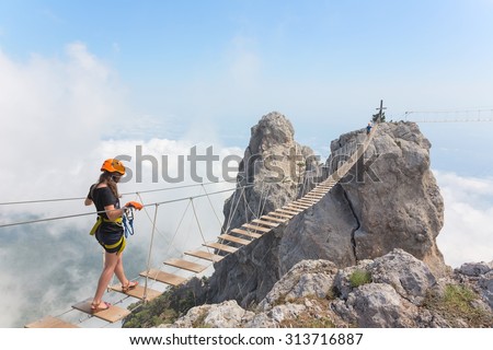 Young woman crossing the chasm on the rope bridge