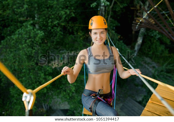 Young woman crossing the chasm on the rope
bridge. Sports entertainment in the
park.