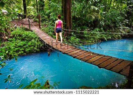 Young woman crossing a hanging bridge in the Jungle of Costa Rica. The river (rio celeste in tenorio national park close to Bijagua) has an emerald green color, caused by volcanic minerals