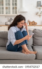 Young Woman Cry Reading Bad News Email, Break Up Message From Ex-boyfriend On Smartphone Sitting Lonely On Couch In Living Room. Depressed Unhappy Female Desperate Of Heartbreak Sms On Mobile Phone