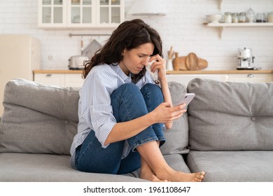 Young Woman Cry Reading Bad News Email, Break Up Message From Ex-boyfriend On Smartphone Sitting Lonely On Couch In Living Room. Depressed Unhappy Female Desperate Of Heartbreak Sms On Mobile Phone