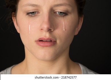 Young woman crying on a black background.