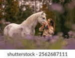 A young woman cuddle and interact with her white spanish horese on a wildflower field in autumn outdoors