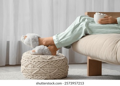 Mujer joven con la taza de cacao que descansa en el sofá en sala de estar