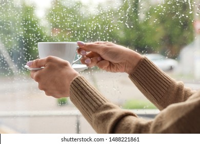 Young Woman With Cup Of Coffee Near Window Indoors On Rainy Day, Closeup