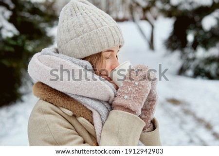 A young woman with a cup of hot tea in mittens. Beautiful winter park. Lots of white snow.