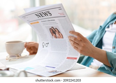 Young woman with cup of tea reading newspaper at home