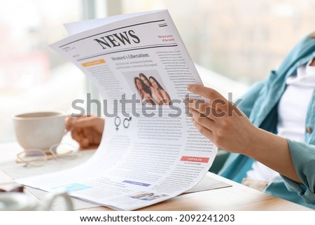 Young woman with cup of tea reading newspaper at home