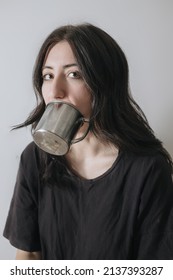 Young Woman With A Cup Of Tea At The Window During Quarantine Wearing Face Mask Worried About The New Lifestyle. Anxiety, Stress, Mental Health, Crisis, Depression, Psychology Therapy.