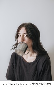 Young Woman With A Cup Of Tea At The Window During Quarantine Wearing Face Mask Worried About The New Lifestyle. Anxiety, Stress, Mental Health, Crisis, Depression, Psychology Therapy.